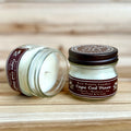 Two 4 ounce glass square mason jar candles with brown lids and labels on a wooden surface. One candle is upright, the other is tilted and open showing the candles white wax. The labels read "Bear Family Candles, Cape Cod Pines" with scent details: cypress bayberry fir. Hand poured soy candle. The lid features a brown bear logo.