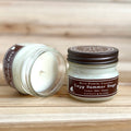 Two 4 ounce glass square mason jar candles with brown lids and labels on a wooden surface. One candle is upright, the other is tilted and open showing the candles white wax. The labels read "Bear Family Candles, Lazy summer Days" with scent details: lemon mint honey. Hand poured soy candle. The lid features a brown bear logo.