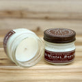Two 4 ounce glass square mason jar candles with brown lids and labels on a wooden surface. One candle is upright, the other is tilted and open showing the candles white wax. The labels read "Bear Family Candles, Winter Bear" with scent details: Eucalyptus, Cypress, Pine. Hand poured soy candle. The lid features a brown bear logo.